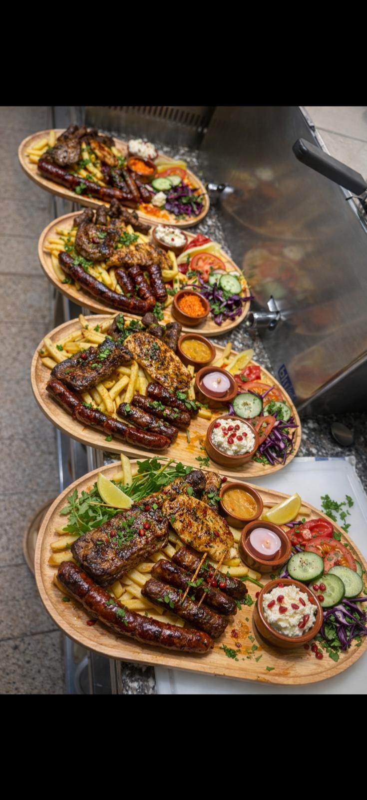 Mehrere reich belegte Grillplatten auf einem Tresen – Troja Grillspezialitäten